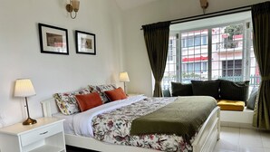 A neatly arranged bedroom with a bed, two bedside tables, a window with curtains, and two framed pictures on the wall. - Hoopoe House (Ootacamund)