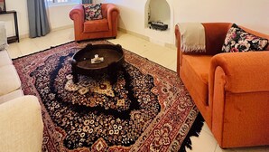 A living room with a sofa, a coffee table, a TV, and a fireplace. - Hoopoe House (Ootacamund)