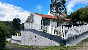 A house with a white picket fence, a red roof, and a large tree in front. - Hoopoe House (Ootacamund)