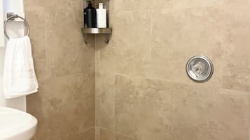 Un espacio de ducha pequeño y cerrado, con azulejos color beige, un lavamanos blanco y un perchero para toallas.