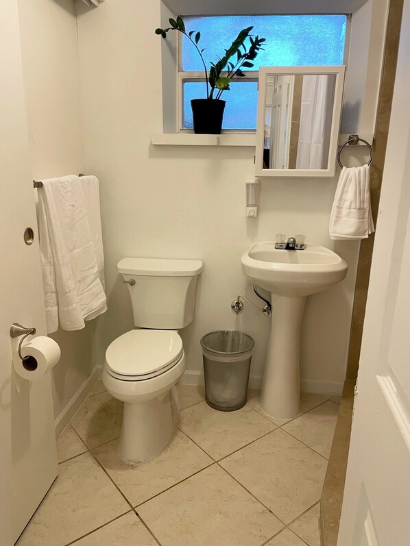 Un baño pequeño y limpio con inodoro, lavamanos y una ventana sobre el lavamanos.