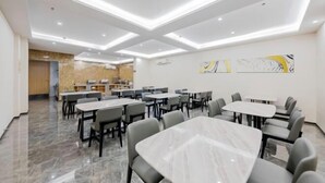 Un'area ristorazione moderna con tavoli e sedie in marmo, illuminazione a soffitto incassata e opere d'arte astratte alle pareti.