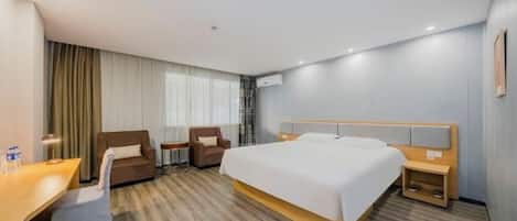 A hotel room with a large bed, a desk, two chairs, and a small table.