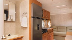 A compact kitchen with a stainless steel refrigerator, wooden cabinets, a sink, and a stove. - Delightful Camper RV Mallard sleeps 4 pool & beach (Panajachel)
