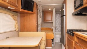 A compact RV kitchen with a stove, microwave, and wooden cabinets. - Delightful Camper RV Mallard sleeps 4 pool & beach (Panajachel)