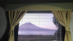 A window with beige curtains, a view of a mountain, and a body of water. - Delightful Camper RV Mallard sleeps 4 pool & beach (Panajachel)