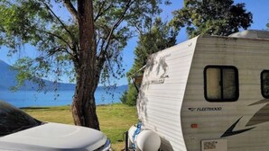 A white RV parked by a lake with trees, a car, and a clear sky. - Delightful Camper RV Mallard sleeps 4 pool & beach (Panajachel)
