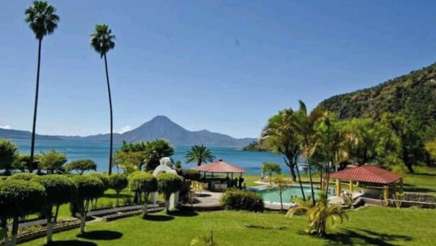 A resort with a pool, palm trees, and a mountain in the background. - Delightful Camper RV Mallard sleeps 4 pool & beach (Panajachel)
