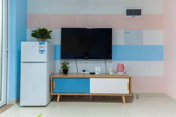Een moderne keuken met een inbouwkoelkast, een flatscreen televisie, een klein kastje en een waterkoker op het aanrecht.