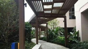 A covered outdoor area with a tiled walkway, surrounded by greenery and a building structure. - Shenzhen Jintaoyuan Hotel Apartment (Shenzhen)