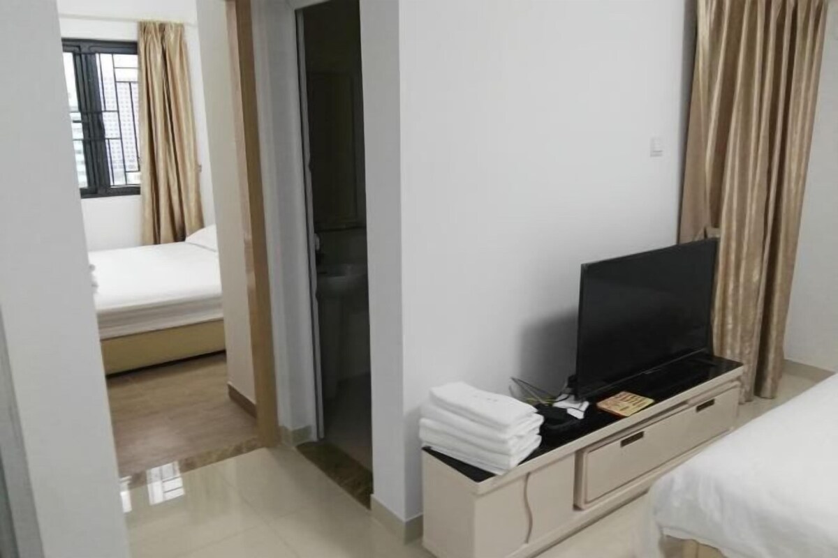 Quarto de hotel com uma cama, uma televisão sobre um suporte e um banheiro visível por uma porta aberta.