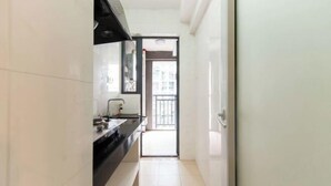 A narrow hallway with a kitchen area on the left, featuring a black countertop and white tiles. - Shenzhen Jintaoyuan Hotel Apartment (Shenzhen)