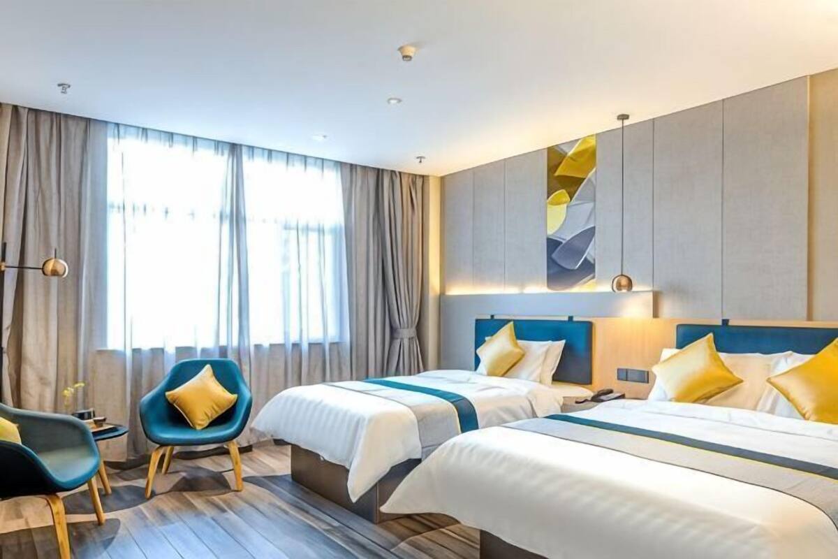 A hotel room with two beds, a desk, a chair, and a large window with curtains.