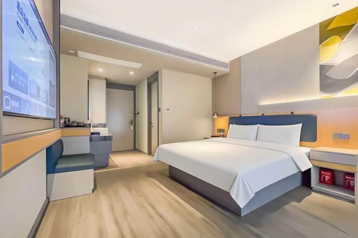 A modern hotel room with a bed, bedside table, TV, and a small seating area.