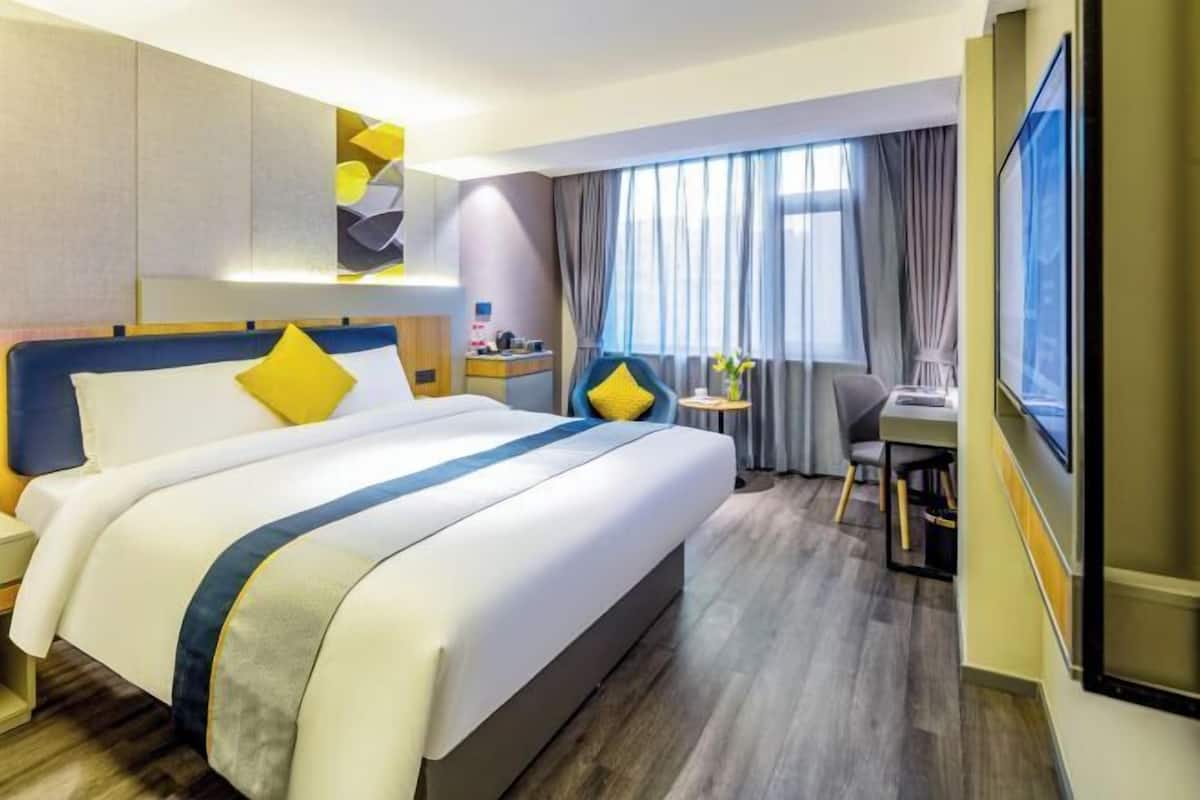 A hotel room with a large bed, a desk, a chair, and a TV.