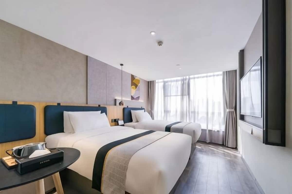 A hotel room with two beds, a desk, a TV, and large windows.