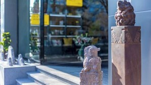 Une statue de lion en pierre, posée sur un piédestal à l’extérieur d’un bâtiment doté d’une entrée en verre.