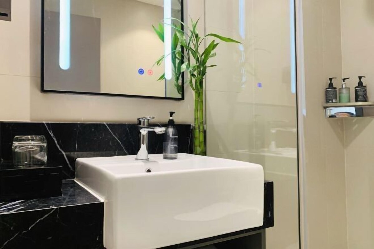 Une salle de bain moderne avec un lavabo blanc, un miroir, une plante en bambou et une douche à parois de verre.