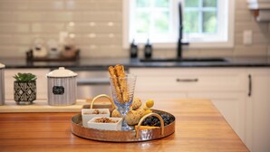 A kitchen counter with a tray of food items including breadsticks, nuts, and berries. There are two containers with labels, one with a geometric pattern and the other with a label that reads "SUGAR". The kitchen has white cabinets and a window in the background. - Hôtel à la maison - La Maison Rouge (Potton)