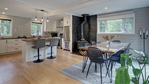 A modern kitchen with a central island, bar stools, and a dining area with a table and chairs. - Hôtel à la maison - La Maison Rouge (Potton)