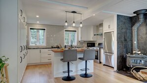 A modern kitchen with white cabinets, a central island with bar stools, a built-in stove, and pendant lighting. - Hôtel à la maison - La Maison Rouge (Potton)
