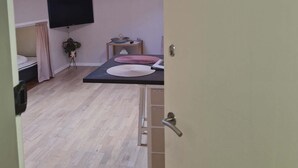 A room with a skylight, a bed, a TV, a small table with a plant, and a sign indicating 'MARIUSTOVA THE COZY ROOM WITH MINI KITCHEN'. - Cosy room with minikitchen in charming Miðvágur, close to the airport. (Miðvágur)