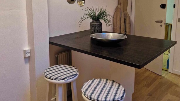 A small kitchen with a dark countertop, two striped stools, a potted plant, and a wall with circular mirrors. - Cosy room with minikitchen in charming Miðvágur, close to the airport. (Miðvágur)