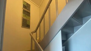 A staircase with a handrail, a small window, and a basket on the landing. - Cosy room with minikitchen in charming Miðvágur, close to the airport. (Miðvágur)
