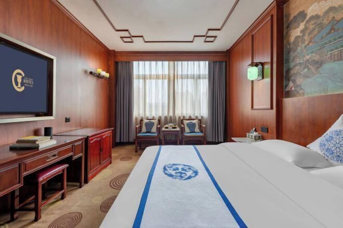 A hotel room with a large bed, a desk, a television, and a painting on the wall.