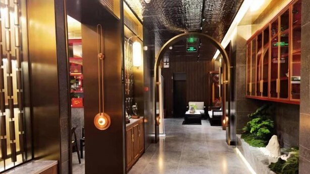 A corridor with a wooden reception desk, a hanging light fixture, and a plant wall.