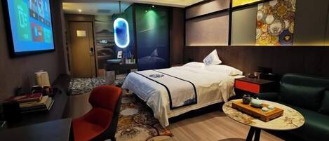 A modern hotel room with a bed, a desk, a chair, and a small table with a tray.