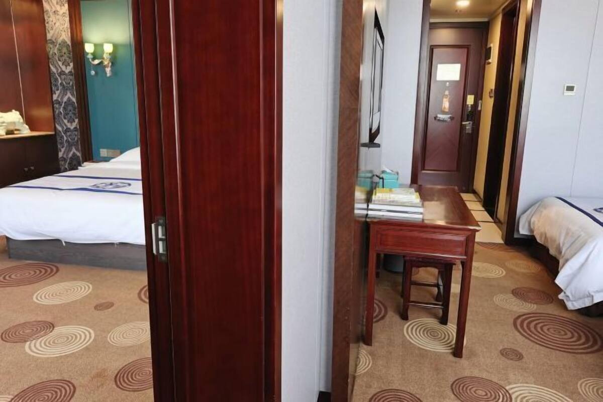 A hotel room with a bed, a wooden desk, and a chair. There is a door leading to another room.