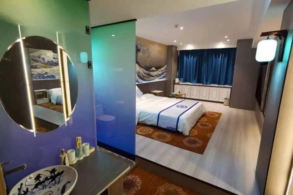 A modern hotel room with a large bed, a round mirror, a sink, and a painting on the wall.