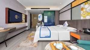 A modern hotel room with a bed, a desk, a TV, and a decorative mirror.