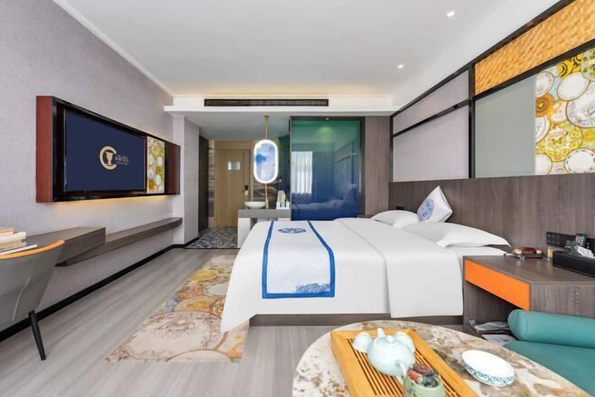 A modern hotel room with a bed, a desk, a TV, and a decorative mirror.