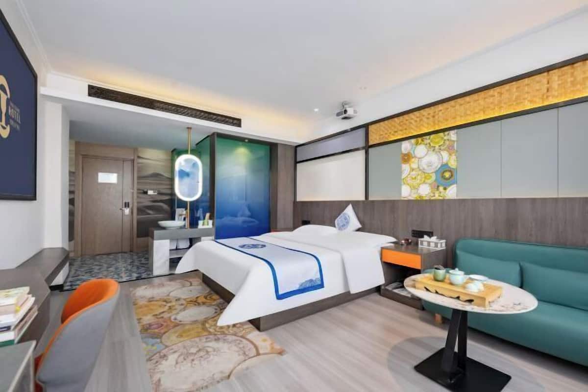A hotel room with a bed, a desk, a sofa, and a small table with a tray of items.