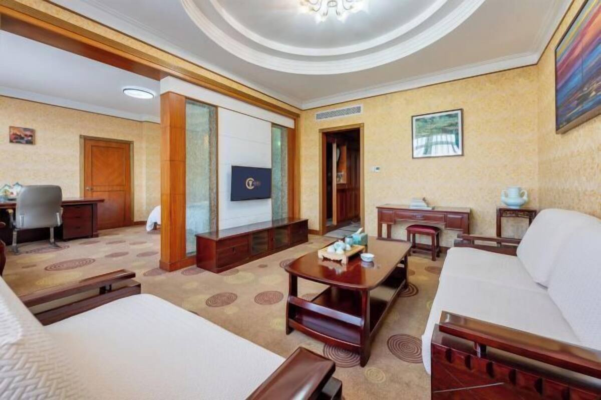 A hotel room with a bed, a desk, a sofa, a TV, and a painting on the wall.