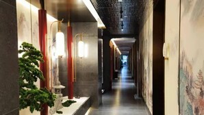 A corridor with a long view, featuring a row of red pillars, a small indoor plant, and a wall with a mural.