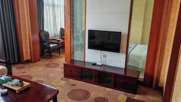 Habitación de hotel con televisor, un mueble de madera, una mesa de comedor con juego de té y una alfombra estampada.