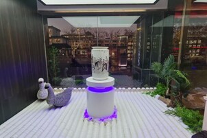 Um jardim interno moderno com um vaso decorativo, uma pequena escultura e um vaso cilíndrico.