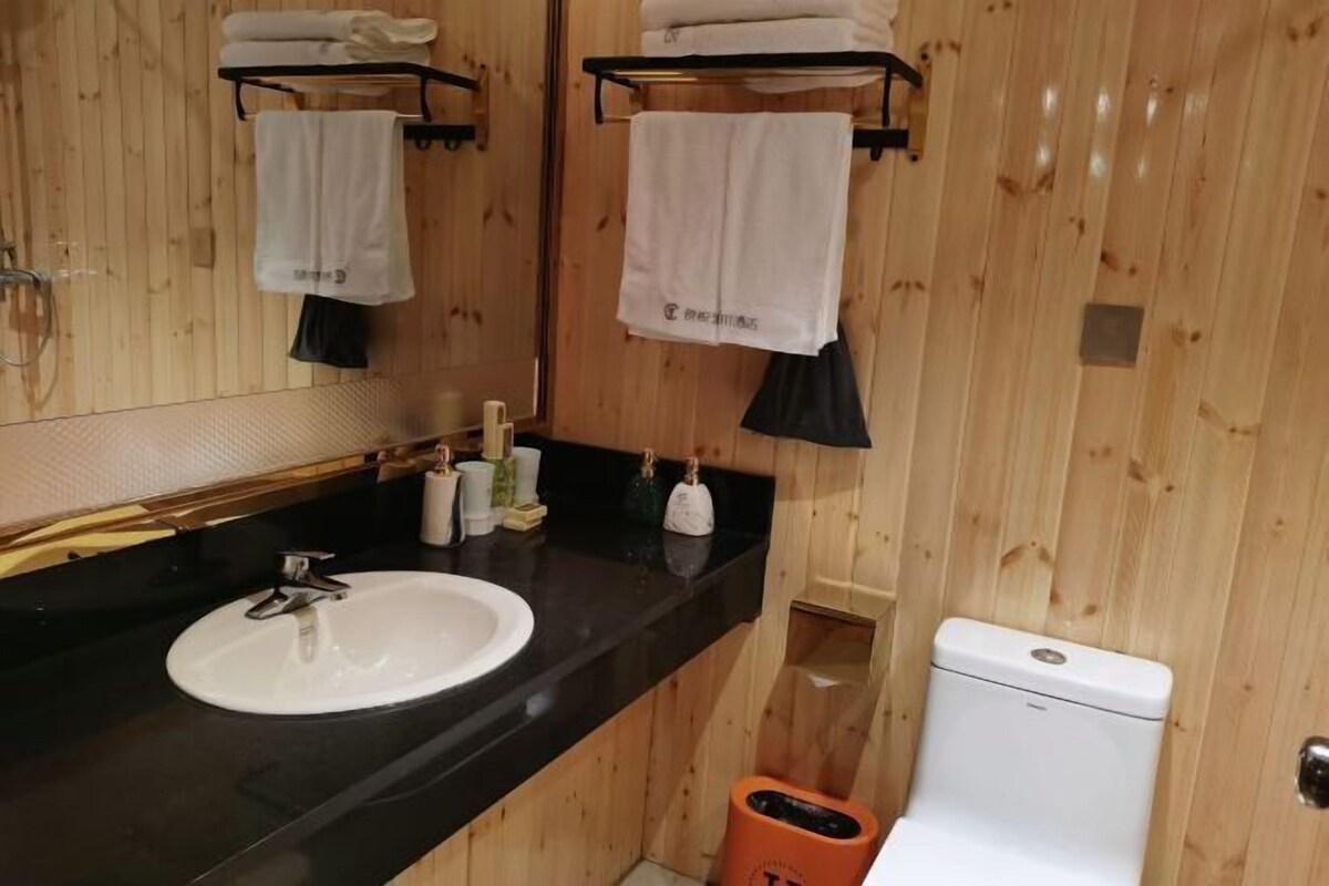 Een badkamer met houten lambrisering, een witte wastafel, een zwart aanrecht en een toilet.