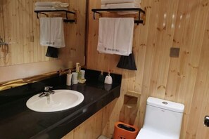 Een badkamer met houten lambrisering, een witte wastafel, een zwart aanrecht en een toilet.