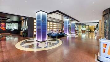 A spacious lobby with a central seating area, a reception desk, and a modern design with illuminated pillars.
