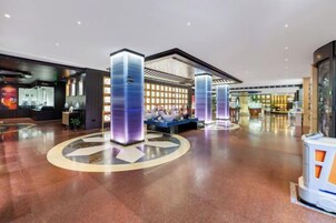 Un vestíbulo amplio con una zona de estar central, una recepción y un diseño moderno con pilares iluminados.