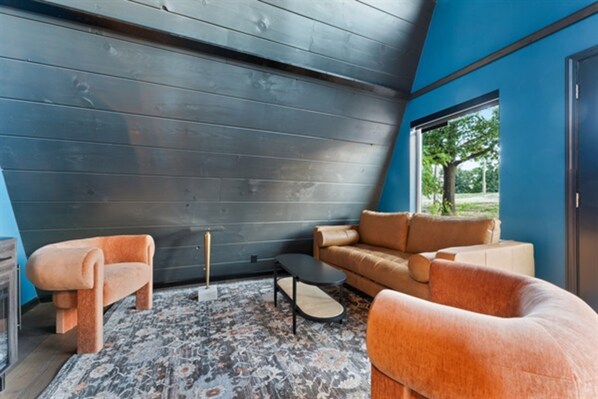 A modern living room with a dark wooden ceiling, a brown leather sofa, a matching armchair, and a patterned rug. - Adults-Only Luxury Cabin w/ Steam Shower + HotTub (Omaha)