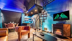 A cozy living area with a fireplace, comfortable seating, and a kitchen in the background.