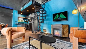 A modern interior with a blue accent wall, a fireplace, a staircase, and a kitchen area.