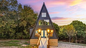 A triangular wooden cabin with a central entrance and a small porch.