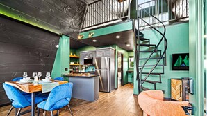 Een moderne keuken met een centraal eiland, een zithoek met blauwe stoelen en een spiltrap.