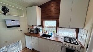 A compact kitchen with a microwave, coffee maker, sink, and stove. - Charming Tiny House Retreat (Olympia)